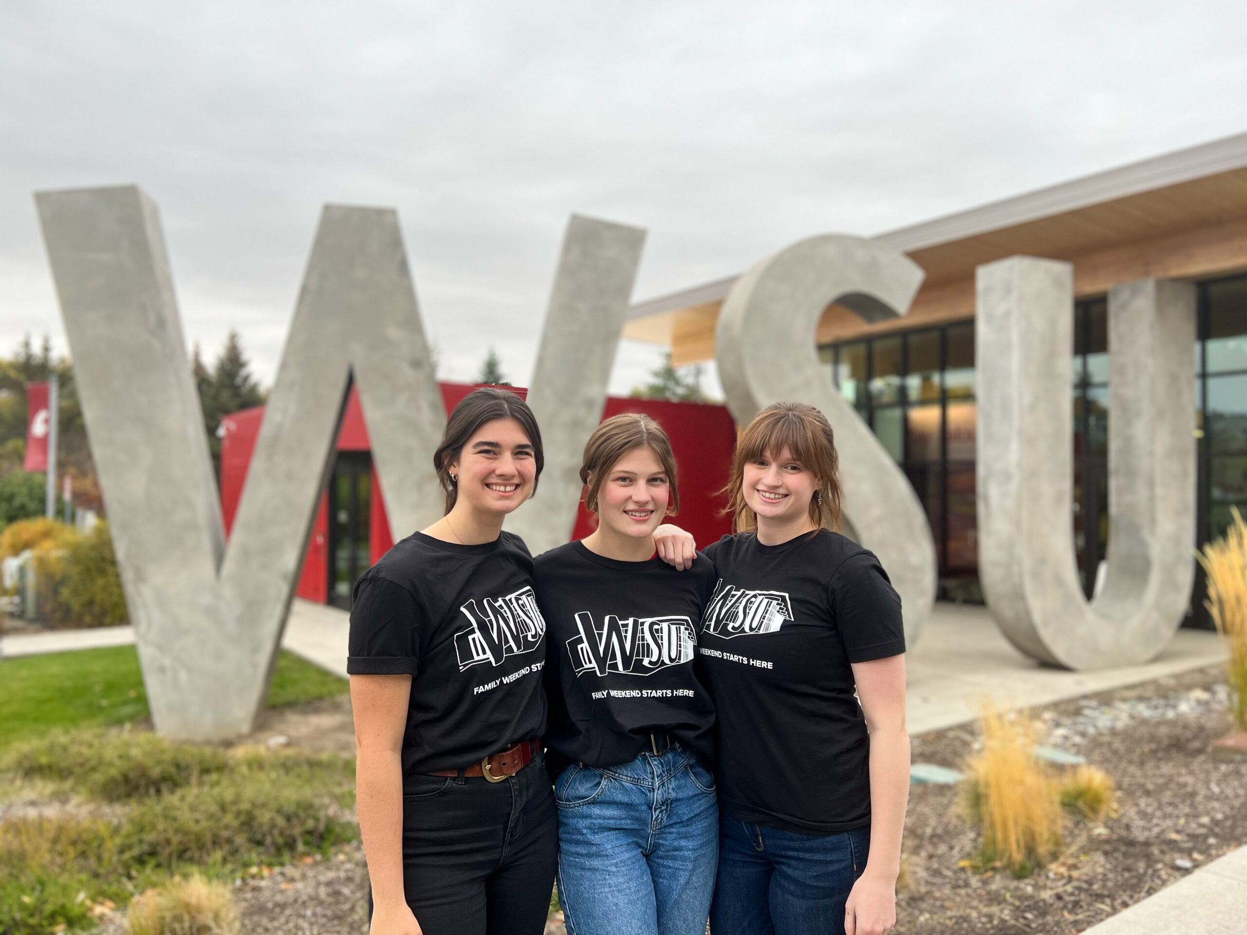 An image of three Brelsford Washington State University Visitor Center employees in front of the facility's W-S-U letters in Pullman, Washington.