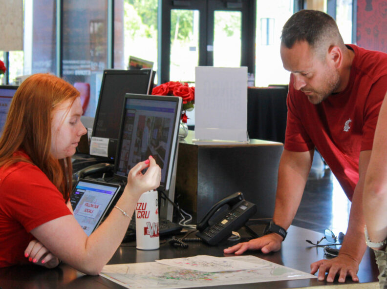 An image of a Brelsford Washington State University Visitor Center employee explaining football weekend parking to a visitor.