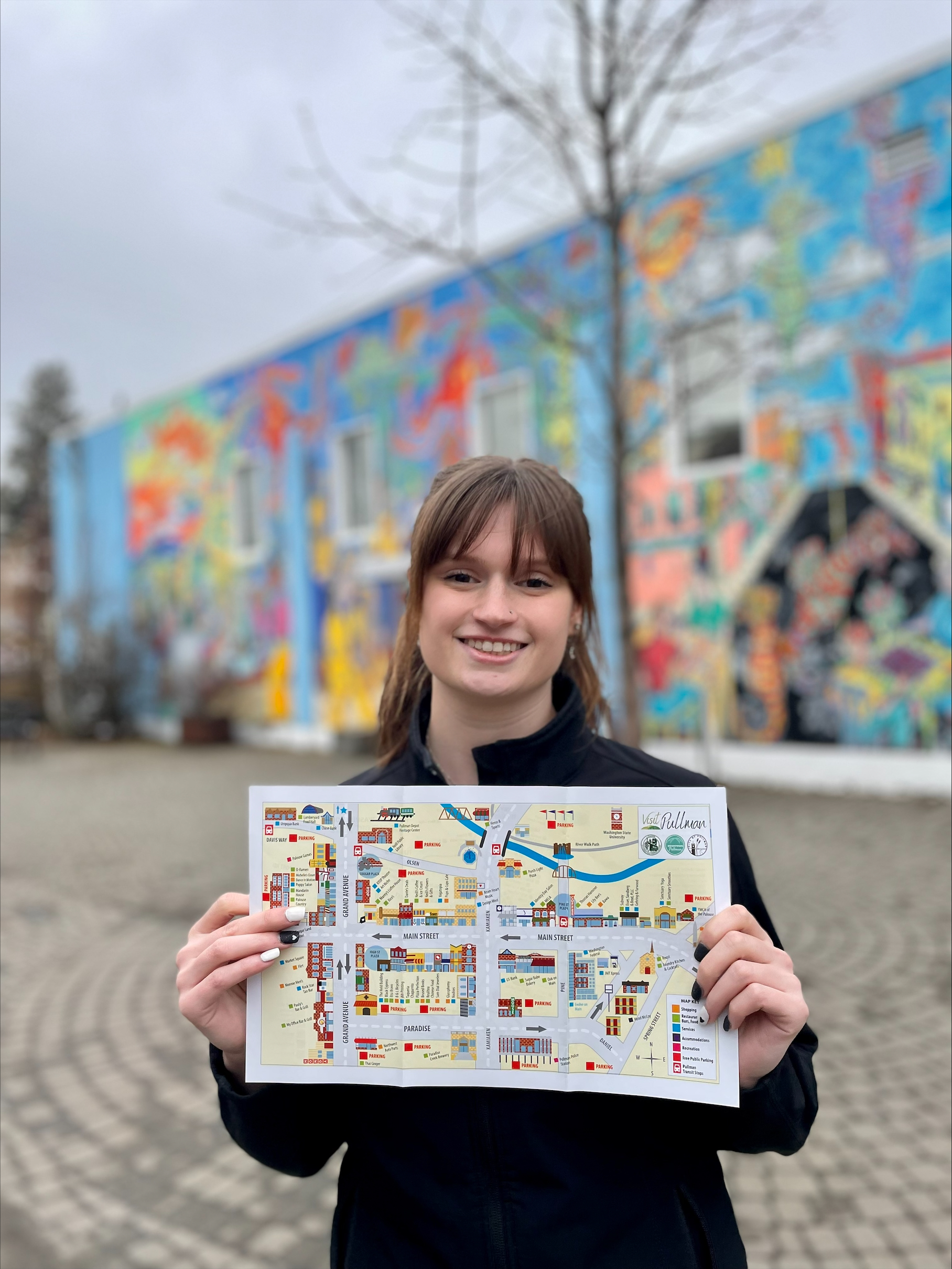 A Brelsford Washington State University Visitor Center employee holding a Downtown Pullman map in a public plaza in Downtown Pullman.