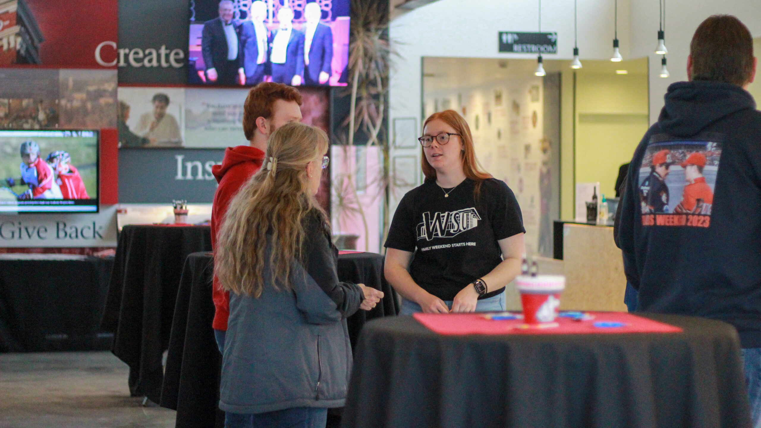 An image of a Brelsford Washington State University Visitor Center employee talking with visitors inside the facility during a campus event weekend.