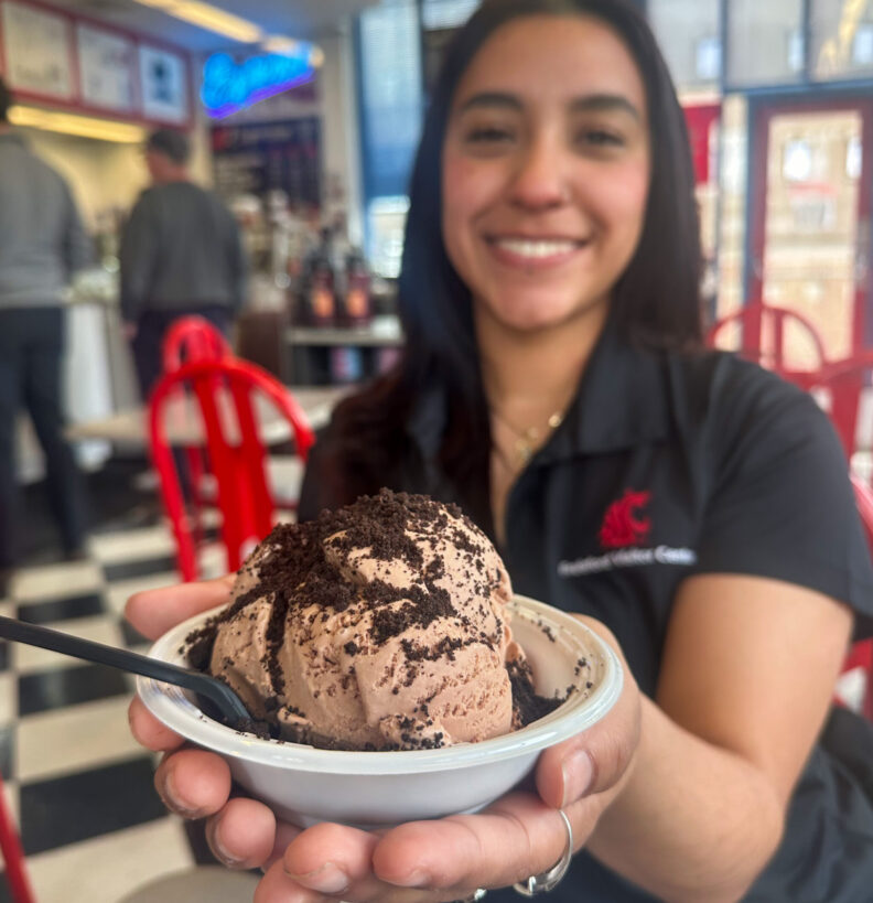 An image of a Brelsford Washington State University Visitor Center employee holding a bowl of chocolate ice cream inside Ferdinand's Ice Cream Shoppe on the WSU Pullman campus.