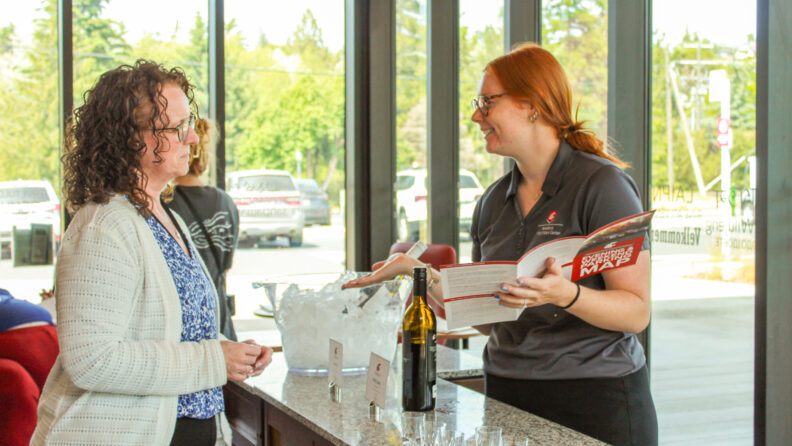 A Brelsford Washington State University Visitor Center employee showing a visitor a campus map during a New Coug Orientation reception at the facility.