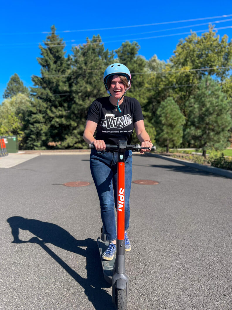 An image of a Brelsford Washington State University Visitor Center employee riding an electric scooter.