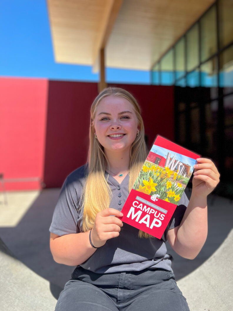 An image of a Brelsford Washington State University Visitor Center employee holding a campus map while sitting outside the facility.