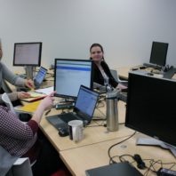 Three women in a computer lab discuss a testing scenario.