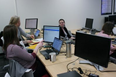 Three women in a computer lab discuss a testing scenario.
