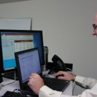 A man smiles while looking at three computer screens.
