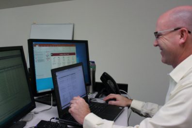 A man smiles while looking at three computer screens.