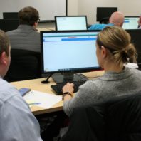 A woman at a computer runs a testing scenario of the Workday system for WSU while a member of the Modernization Team looks on.