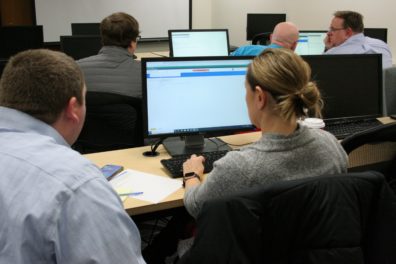 A woman at a computer runs a testing scenario of the Workday system for WSU while a member of the Modernization Team looks on.