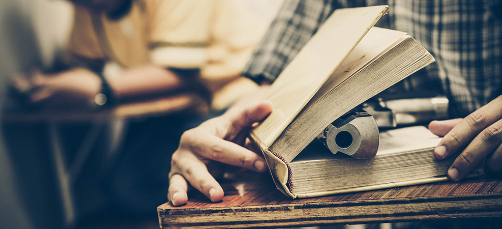 picture of a gun barrel sticking out of a book on a desk in a classroom
