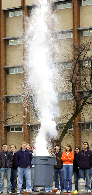 Image of a volcanic eruption demonstration - a trash can surrounded by students with an obvious eruption rising into the sky.
