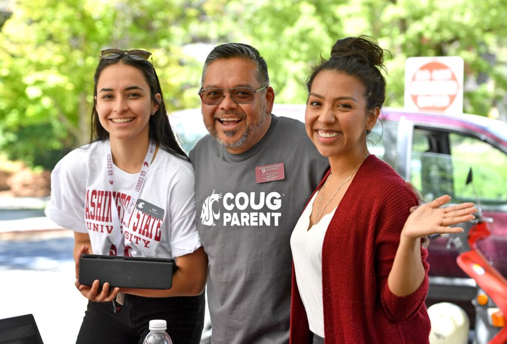 A student poses with their parents outdoors in summer.