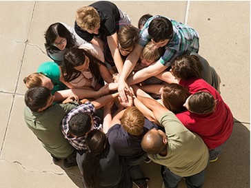 An overhead shot of a group of students all putting their hands in for a cheer.