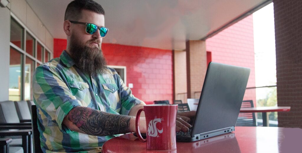 A student in sunglasses works on a laptop inside the Compton Union Building.