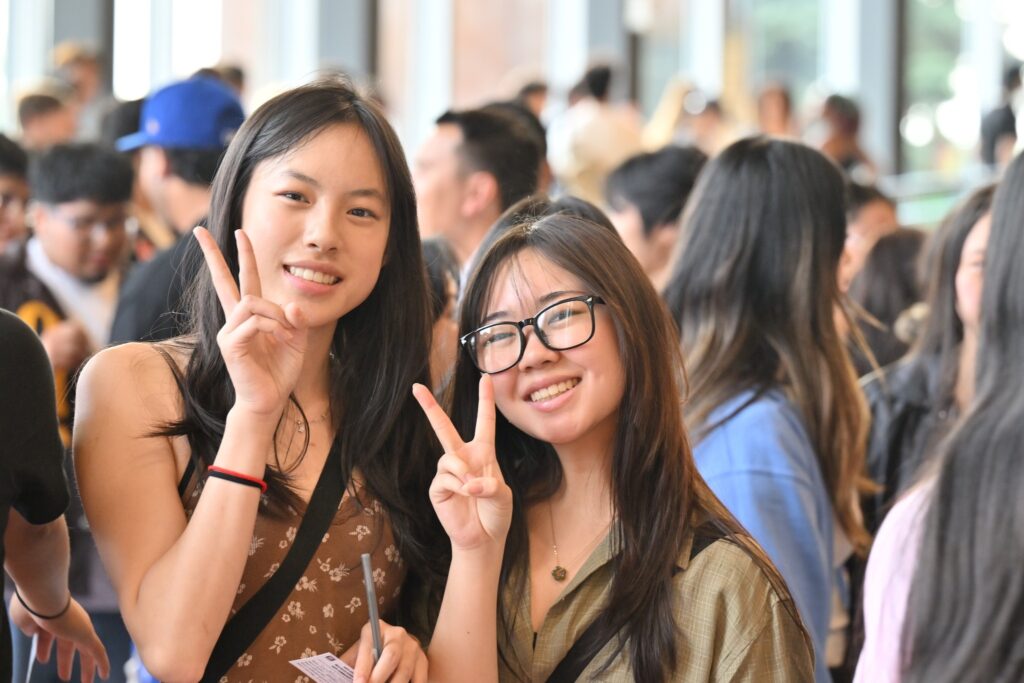 Two students give peace signs while standing outside a building on the WSU Pullman campus.