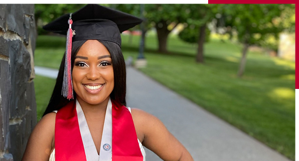 A graduating student in a cap and gown poses outside on WSU Pullman campus
