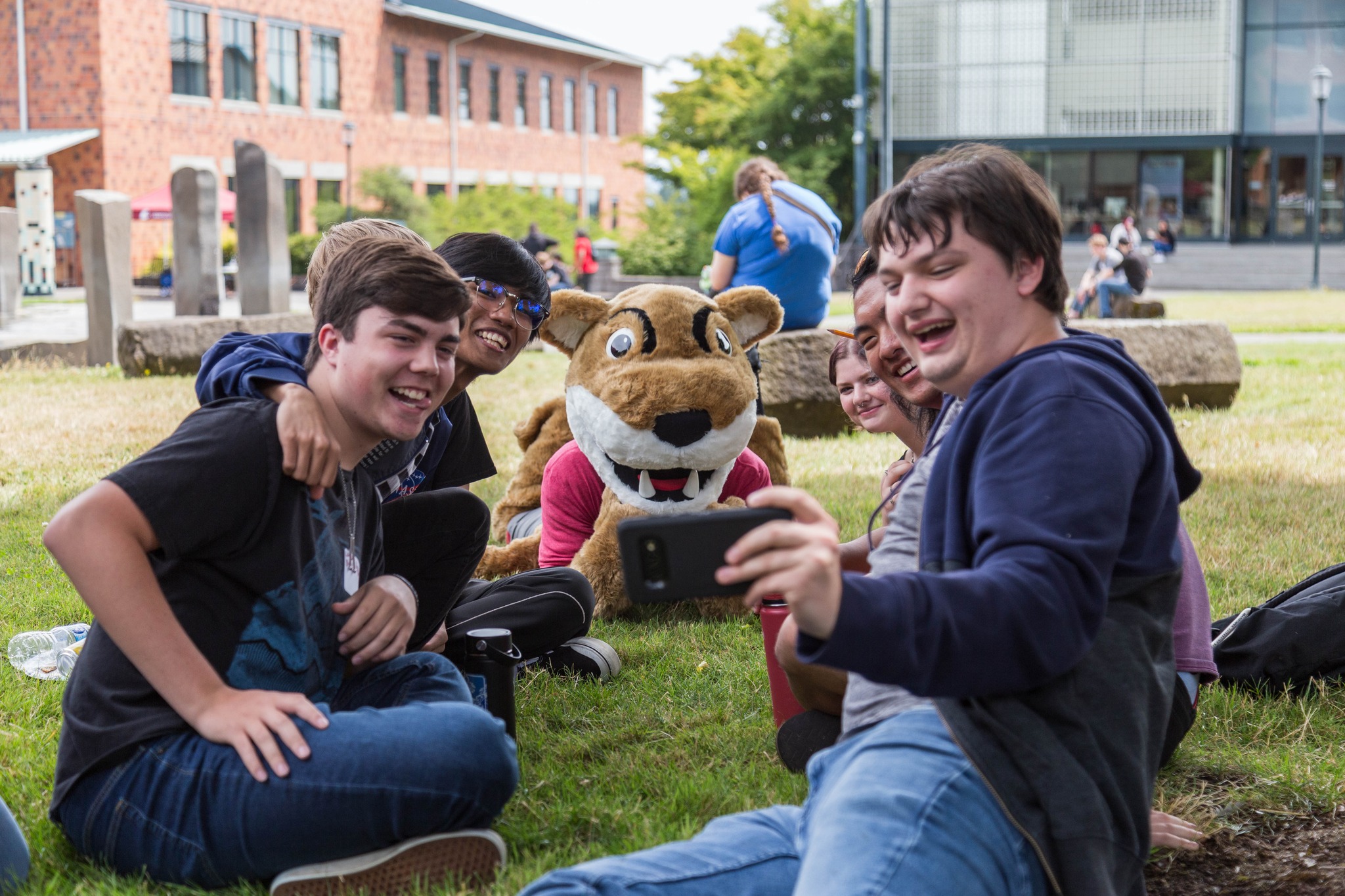 Two students poses outside on the grass with Butch T. Cougar.