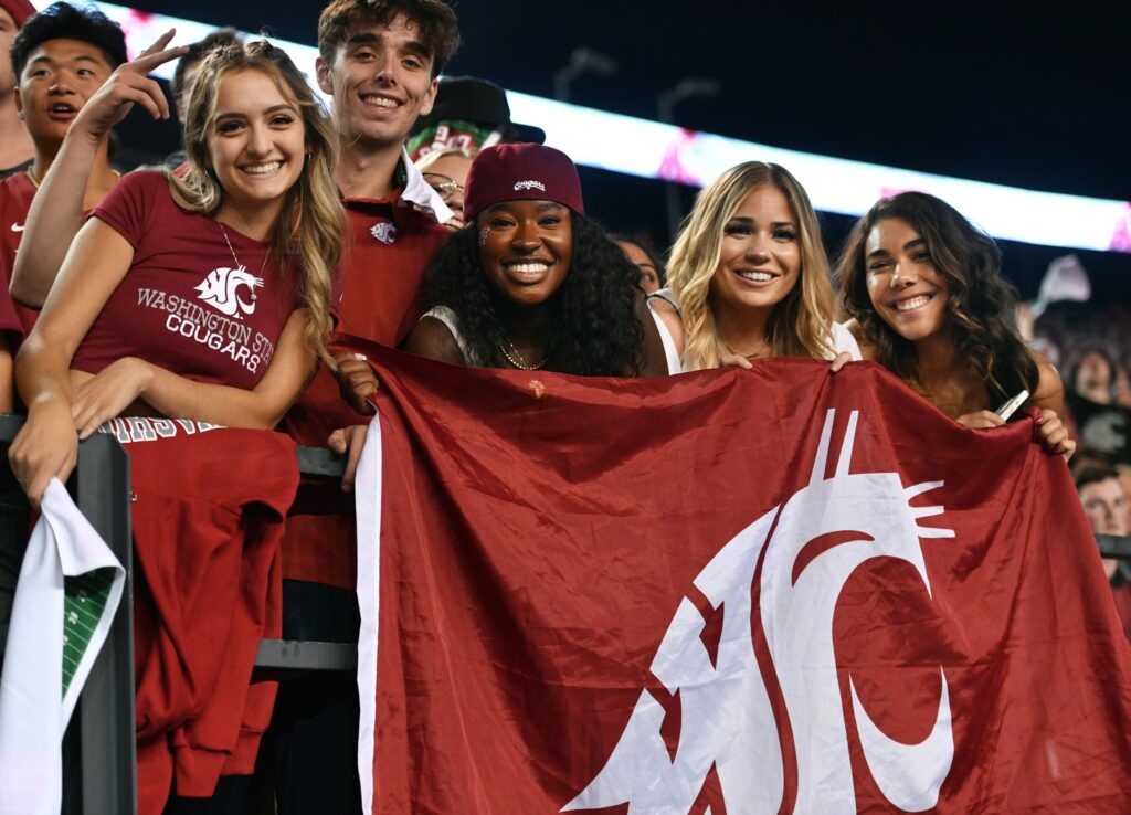 Students pose with the WSU flag at a sports event.