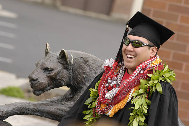 A graduating student poses next to the cougar statue outside the WSU Alumni Center.