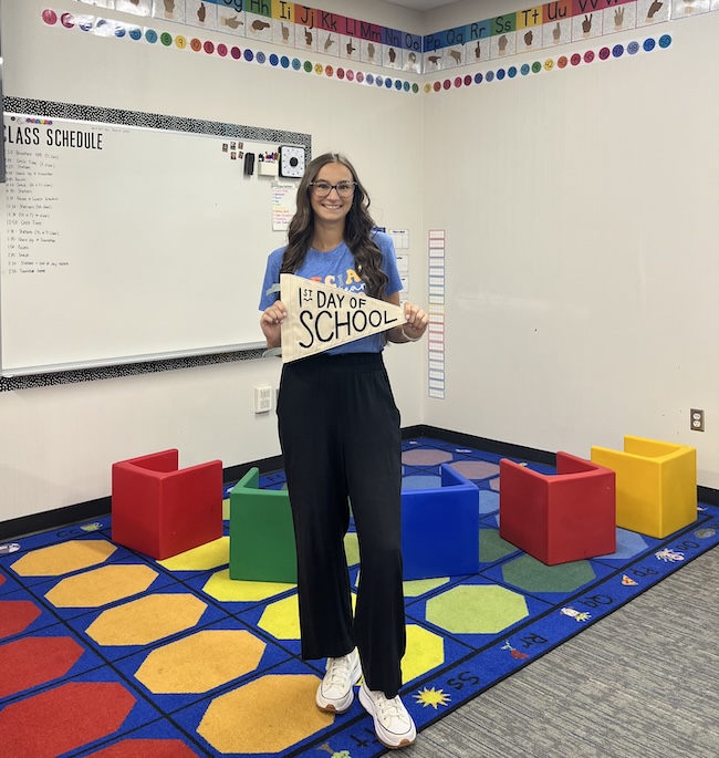 Lexi Brantner standing in a classroom with a "first day of school" sign