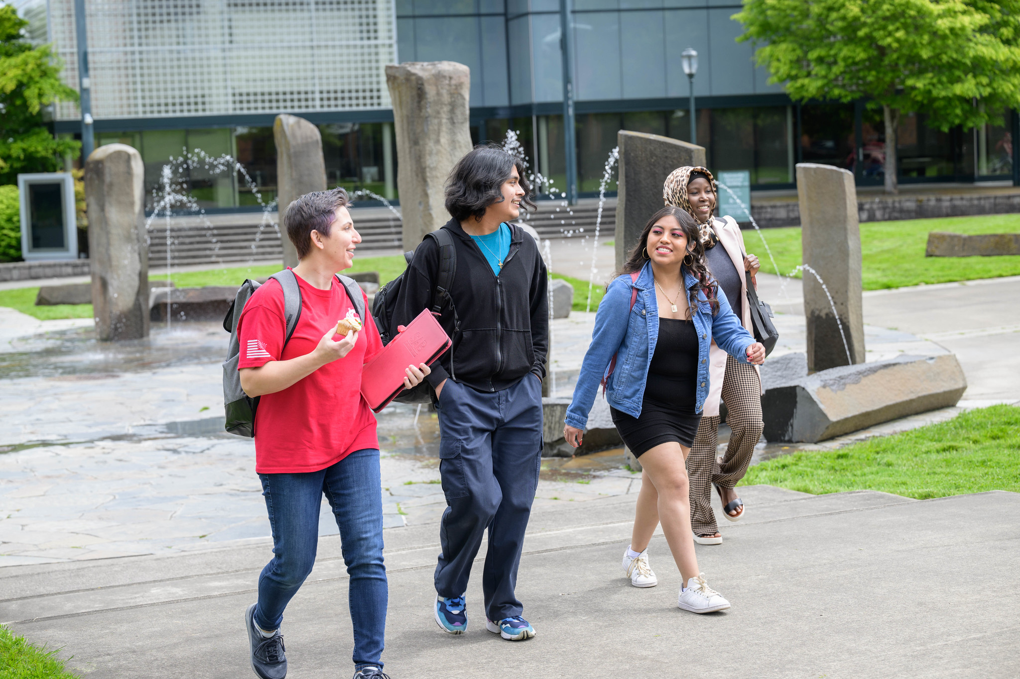 Four students walk on campus, with two smiling at each other