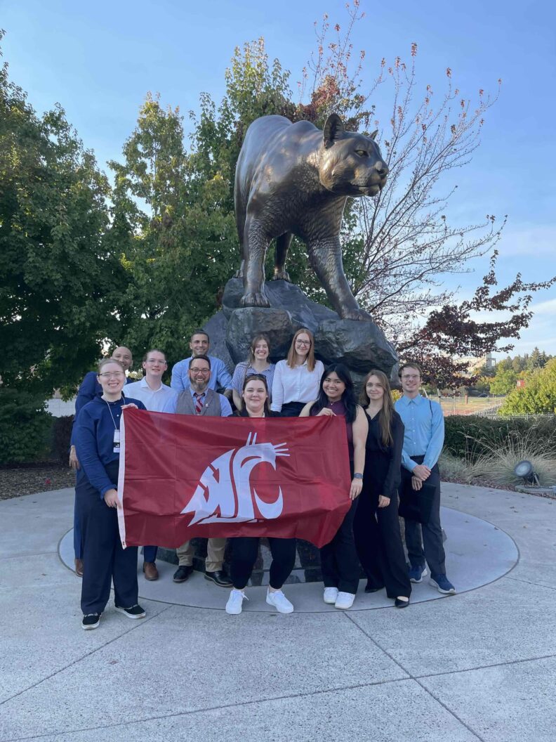 Camille Orego (center) holds the WSU flag with her SWE Club in front of the Cougar Pride statue. 