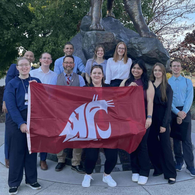 Camille Orego (center) holds the WSU flag with members of the Society of Women Engineers (SWE) in front of the Cougar Pride statue.