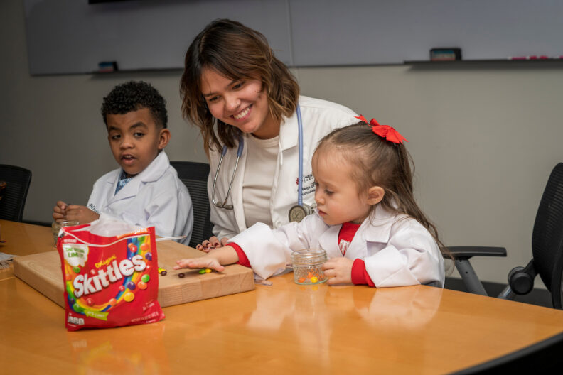 Two kids and an instructor practice pharmacy work.