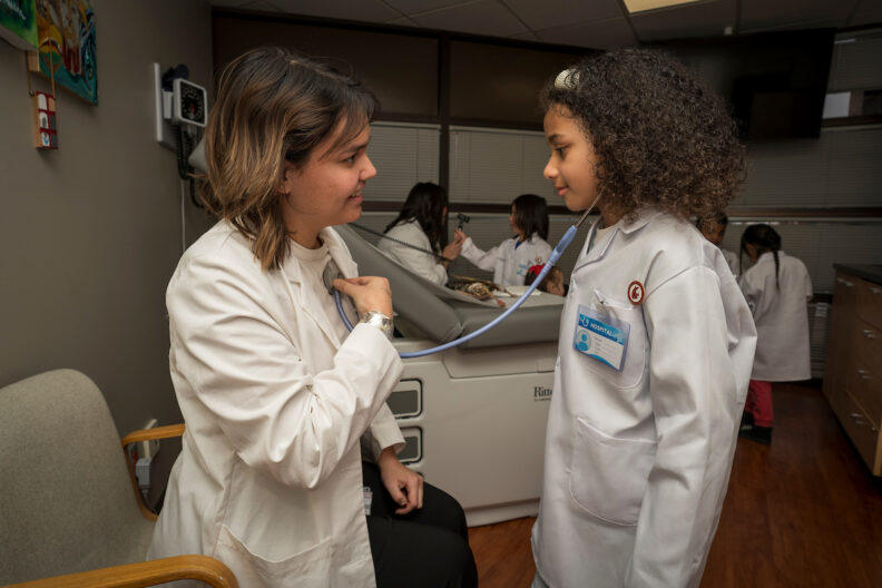 A child listens to an instructor's heart using a stethoscope.