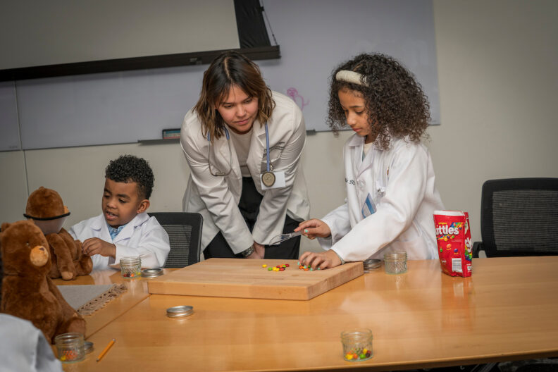 Two kids and an instructor practice pharmacy work.
