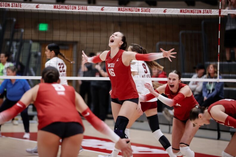 Washington State University volleyball player Lucie Blazkova (No. 16) throws her arms wide in celebration after a point, her mouth open in a cheer, as teammates react around her during a home match against Santa Clara.