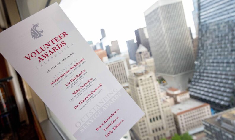 A printed Volunteer Awards Celebration program, dated Seattle, WA, May 14, 2026, held up in front of a window overlooking the Seattle skyline.