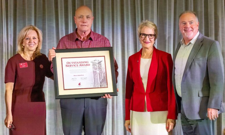 From left, WSU Foundation board director Liz Pritchard, honoree Bruce Amundson, WSU President Betsy Cantwell, and WSU Foundation CEO Mike Connell on stage as Amundson holds his framed Outstanding Service Award at the 2026 Volunteer Awards Celebration.