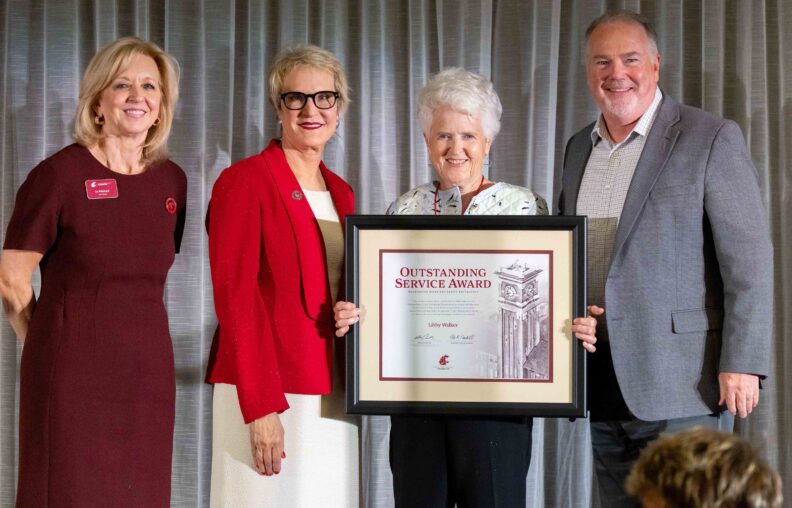 Libby Walker holds her framed Outstanding Service Award certificate on stage with three WSU Foundation representatives at the 2026 Volunteer Awards Celebration.