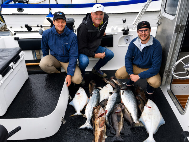 Brad Crollard poses aboard a fishing boat with two international interns and a display of fish caught during a fishing trip.