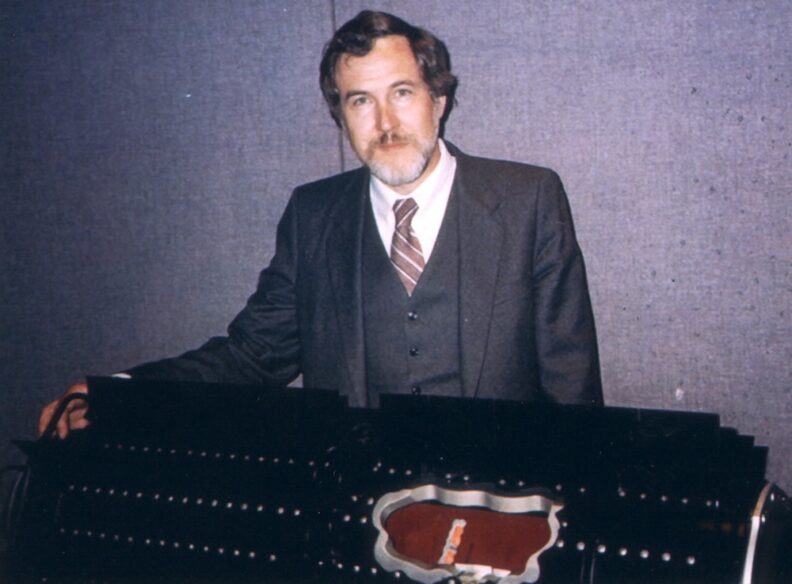 Gary Bennett sits at a table with a cutaway model of the General-Purpose Heat Source Radioisotope Thermoelectric Generator.