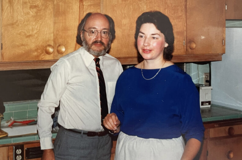 Dr. Roy Filby stands beside another person in a kitchen with wooden cabinets and tiled countertops.