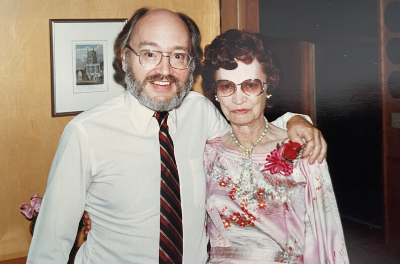 Dr. Roy Filby stands with an older attendee wearing a pink floral dress and corsage.