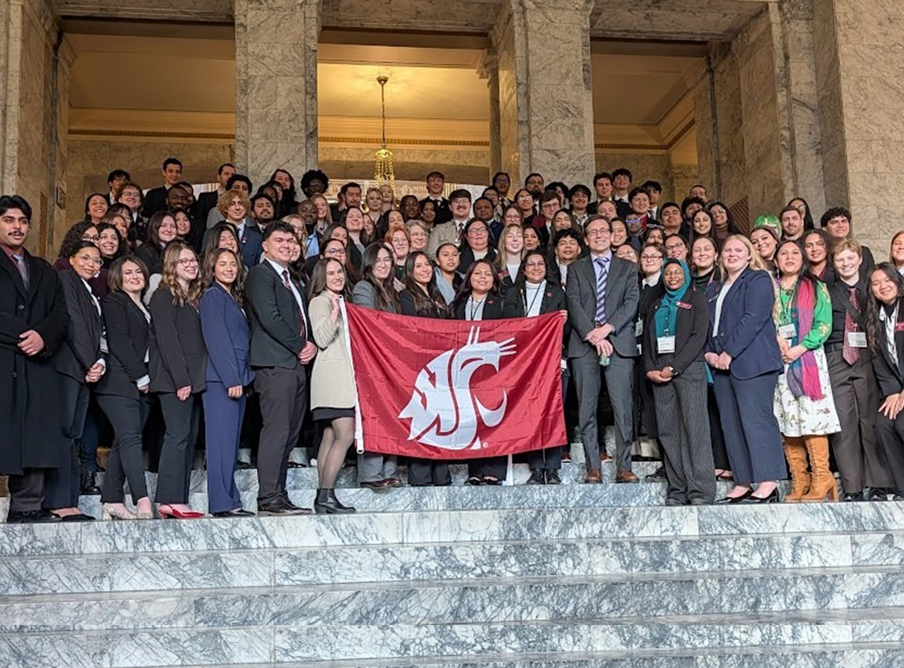 Crowd of WSU students in from of Washington State Capitol building holding WSU Cougar flag. 