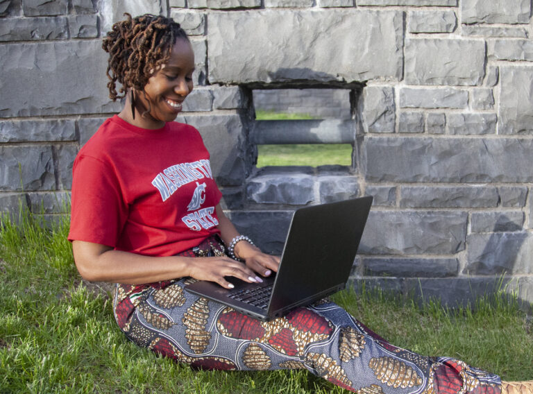 Smiling woman on laptop waring WSU t-shirt