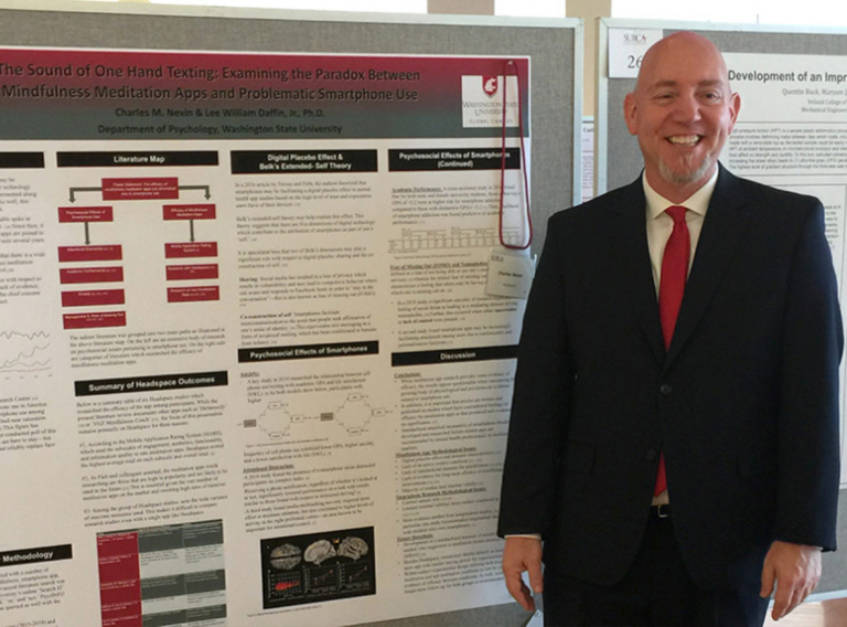 Smiling man in suit presenting academic research on poster board.