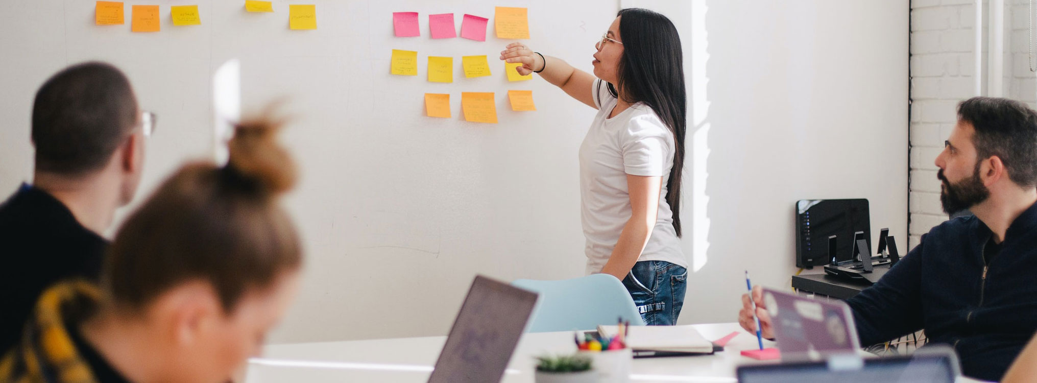Photo: Woman points to sticky notes on whiteboard.