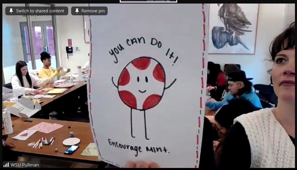 Pullman student holding up a handmade card that says “You can do it!”