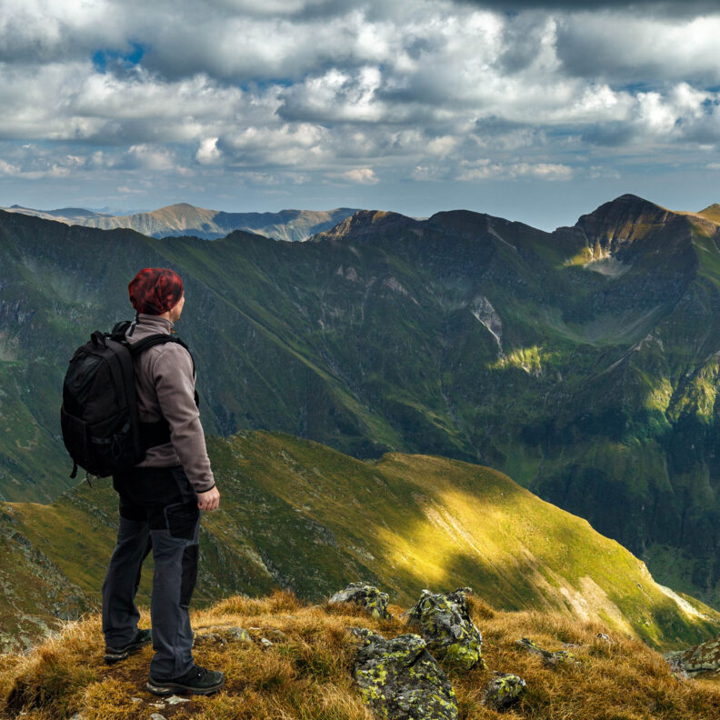 Photo of hiker standing in front of scenic mountain range.
