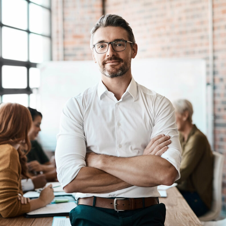 Photo of man in business attire standing with arms crossed, looking at camera