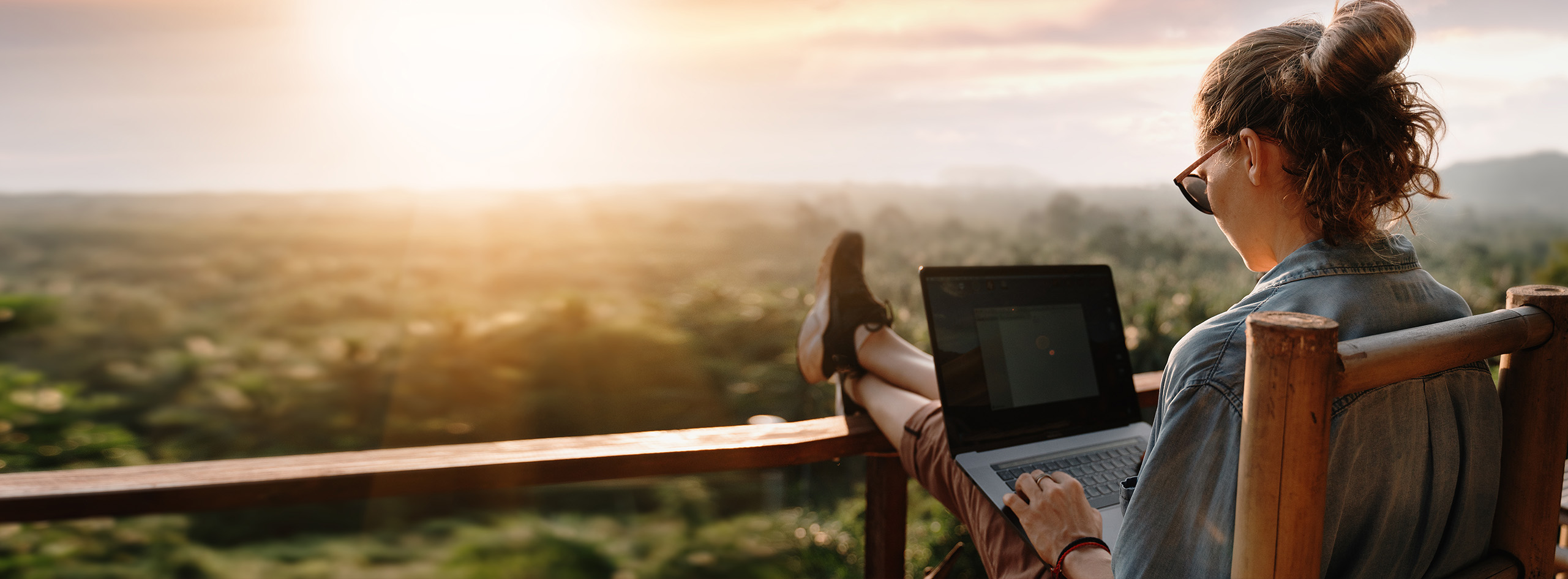Photo of woman on laptop watching sunset