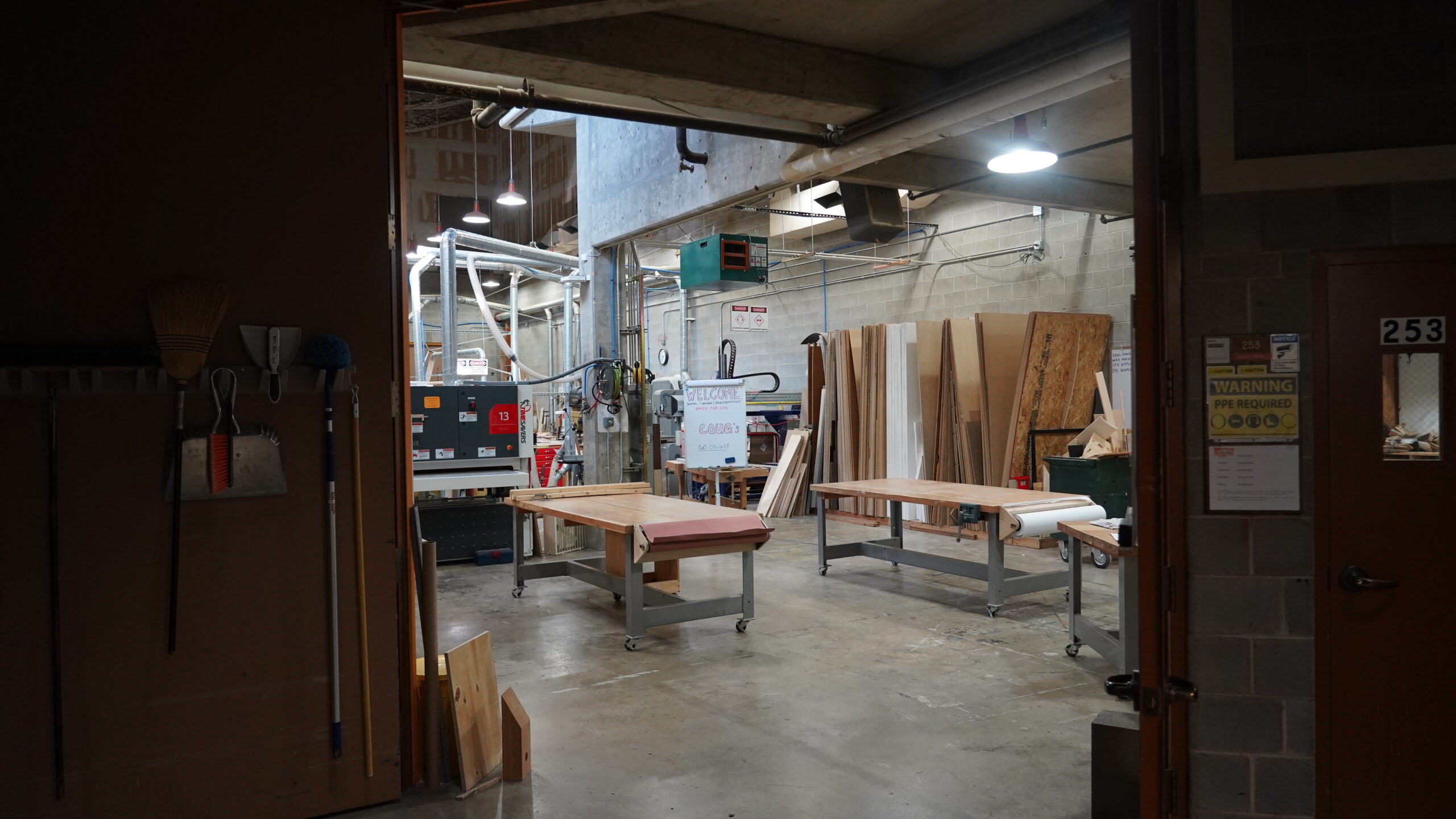 Image of a woodshop taken from the hallway looking inside. Wood materials and machines shown.