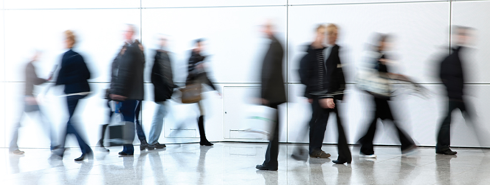 Blurred image of people walking in a modern hallway, representing movement, management, and business dynamics.
