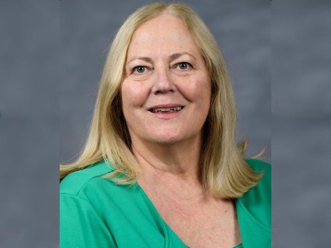 Portrait of a smiling woman with blond hair wearing a green shirt.